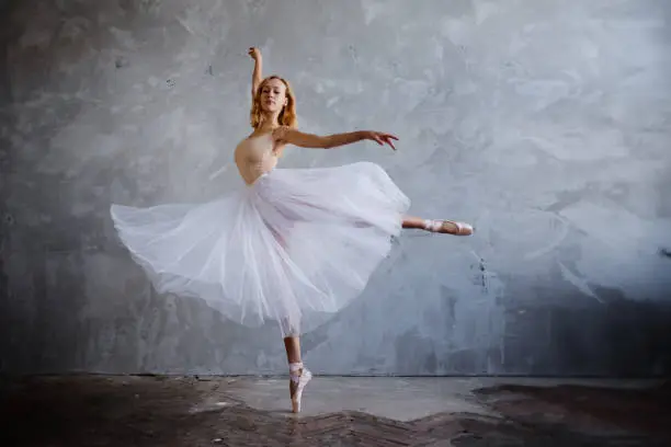 Young and slim ballet dancer is posing in stylish studio with big windows