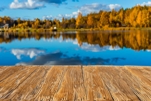 istock Empty rustic wood table top on  blurred colorful autumn landscape background with fall forest and blue sky with cloudscape reflection on the lake. Can montage or display your products 881114778