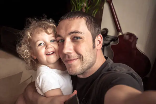 Photo of Cheerful father embracing daughter making family selfie