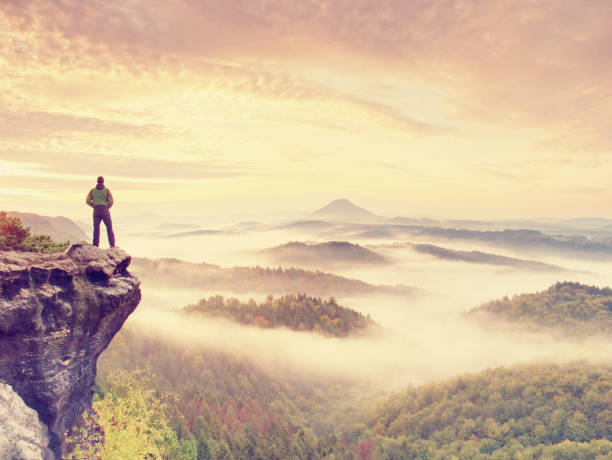 istock Man stay on rocky peak within daybreak and watch over misty landscape. 881146512