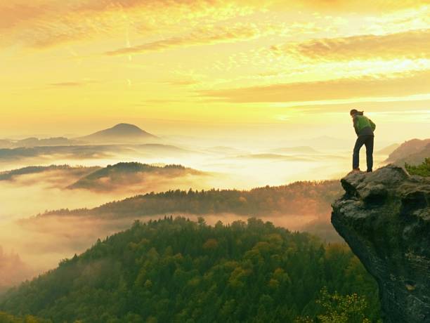 istock Man stay on rocky peak within daybreak and watch over misty landscape. 881146590