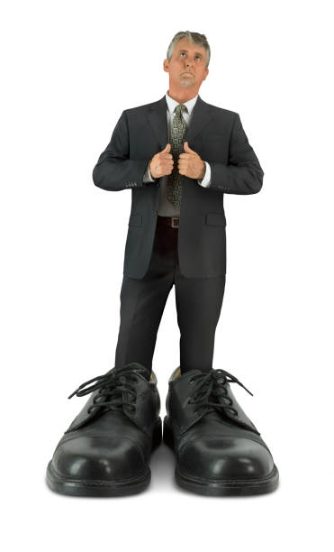 Some big shoes to fill man standing in giant shiny business footwear stock photo