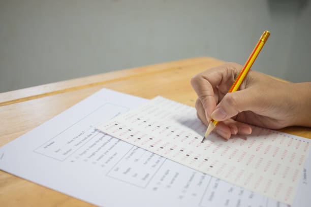 istock Students hands taking exams, writing examination room with holding pencil on optical form of standardized test with answers and english paper sheet on row desk chair doing final exam in classroom. 881191994