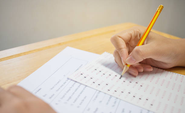 istock Students hands taking exams, writing examination room with holding pencil on optical form of standardized test with answers and english paper sheet on row desk chair doing final exam in classroom. 881192080
