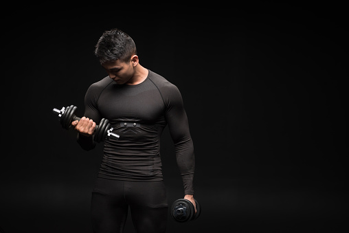 muscular asian man in sportswear exercising with dumbbells isolated on black