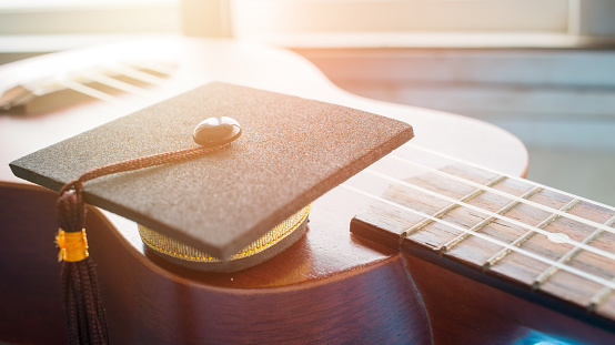 Graduation cap Put on ukulele, a small instrument. The ukulele is member of lute family of instruments with nylon stringed, usually played with bare thumb or fingertips. Concept of Music Education.
