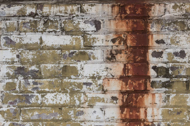istock Peeling white and green painted brick wall with a large band of dripping rust stains 881298092