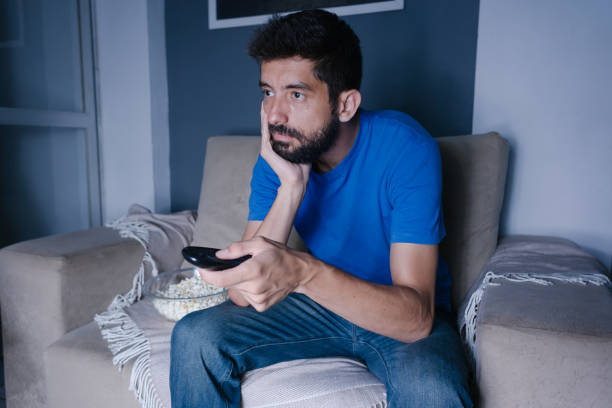 istock Bored man watching tv on the couch at night 881305872