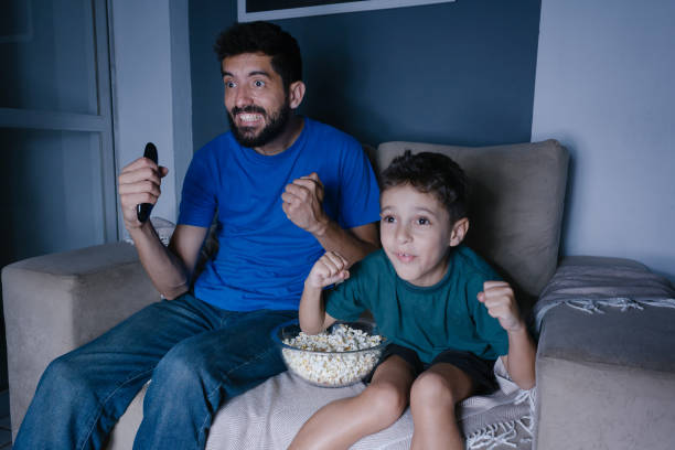 fahter e il figlio guardano la tv e tifano di notte - little boys people indoors soccer foto e immagini stock