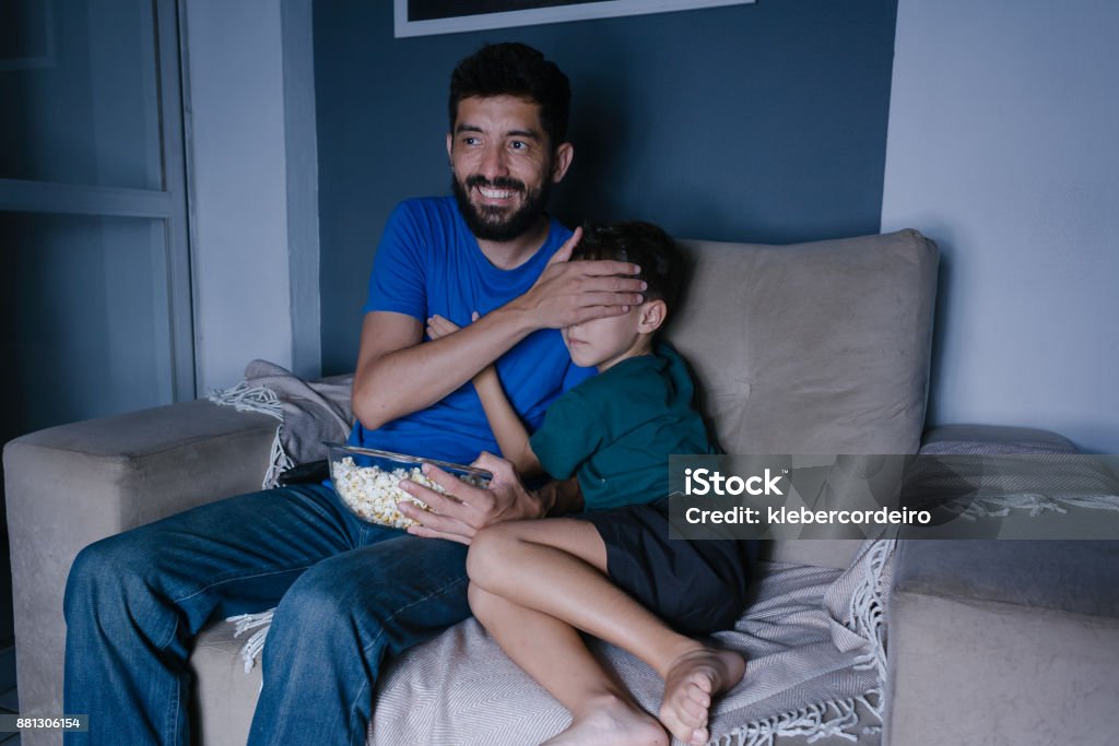 Padre e hijo viendo scary movie en la tv por la noche. Padre que cubre los ojos de su hijo - Foto de stock de Adulto libre de derechos