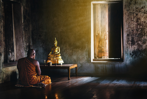 A monk is worshiping and meditating in front of the golden Buddha as part of Buddhist activities.Focus on the monk