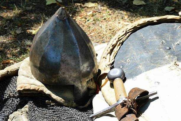 istock Spiky conical norman type casque helmet with nose protection placed on chainmail armor, there is also handle of longsword visible 881381392