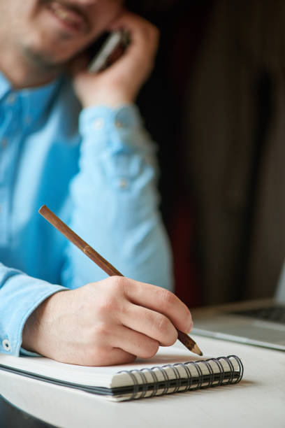 istock Young man writes data to a notebook by talking on the phone 881436410