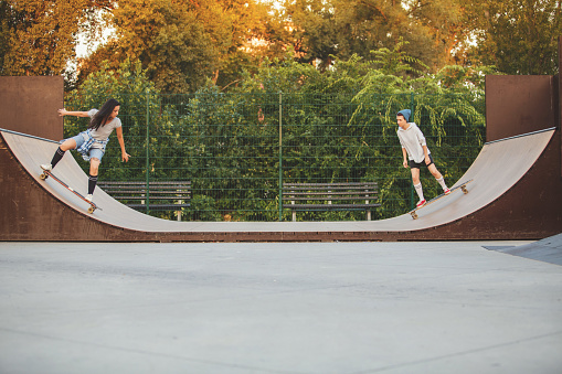 Two young women are skating down in bowl in skateboard park. They are practicing their skateboard skills.