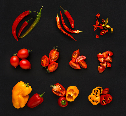 Collage of assorted red vegetables isolated at black background. Fresh raw whole and cut cooking ingredients. Chilli and bell pepper, cherry tomatoes top view
