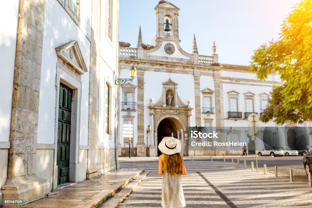 Woman traveling in Faro town on the south of Portugal Young woman tourist standing on the city gate background in Faro town on the south of Portugal Faro City - Portugal Stock Photo