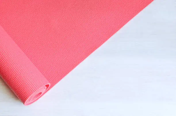 Open pink exercise mat on white wooden background.  Concept for practice yoga, pilates or any  physical workout.