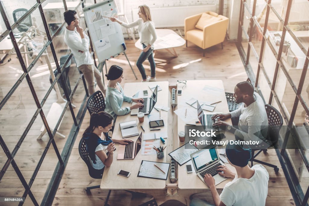 Young people work in modern office. Top view of multiracial young creative people in modern office. Group of young business people are working together with laptop, tablet, smart phone, notebook. Successful hipster team in coworking. Freelancers. Office Stock Photo