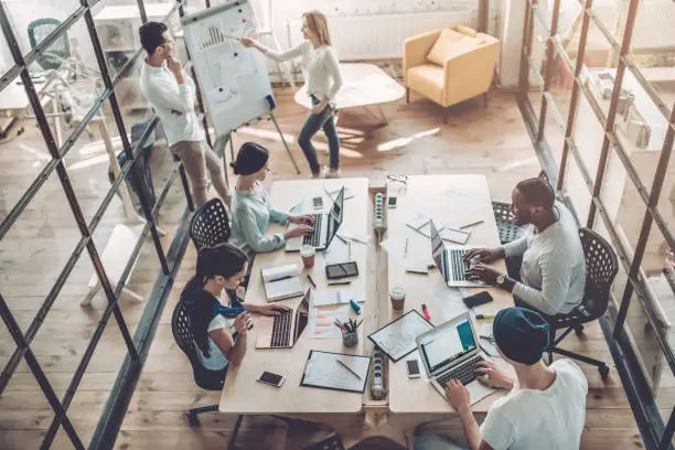 Top view of multiracial young creative people in modern office. Group of young business people are working together with laptop, tablet, smart phone, notebook. Successful hipster team in coworking. Freelancers.