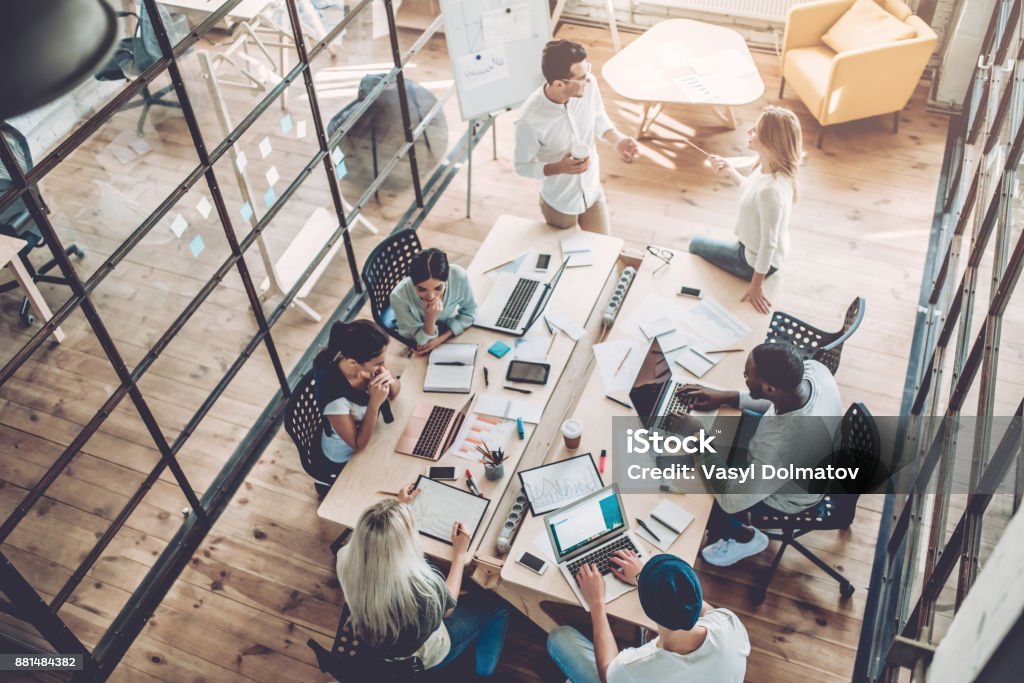Young people work in modern office. Top view of multiracial young creative people in modern office. Group of young business people are working together with laptop, tablet, smart phone, notebook. Successful hipster team in coworking. Freelancers. Office Stock Photo
