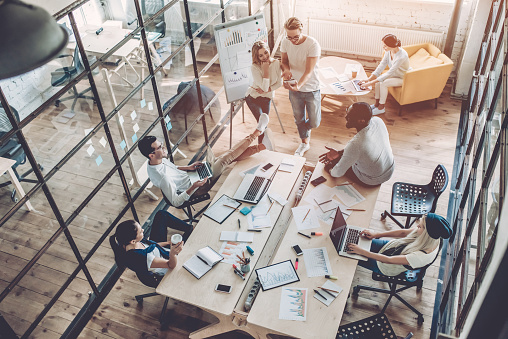 Top view of multiracial young creative people in modern office. Group of young business people are working together with laptop, tablet, smart phone, notebook. Successful hipster team in coworking. Freelancers.