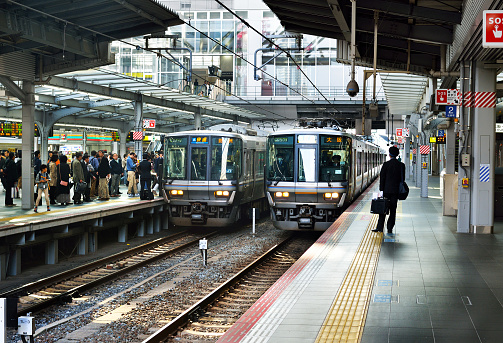Osaka, Japan - November 3, 2017:  Trains departing and arriving at Osaka Station as passengers wait on the platform.