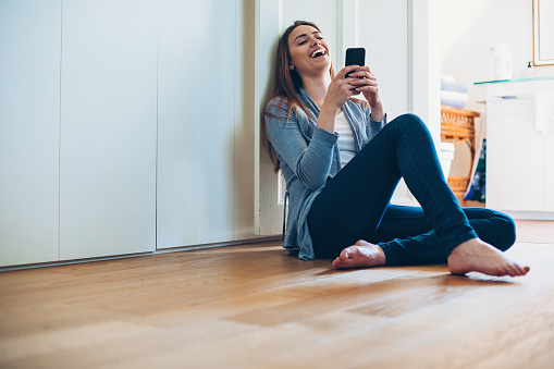Young woman sitting on floor at home with a mobile phone