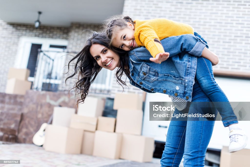 daughter piggyback riding mother happy daughter piggyback riding mother in front of new house Moving House Stock Photo