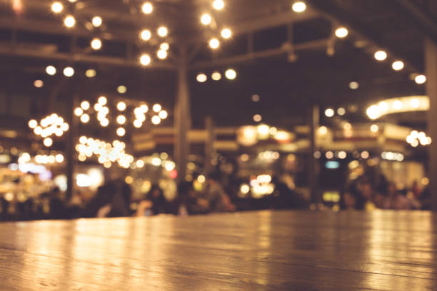 Wood table with blur of lighting in night cafe Wood table top with reflect on blur of lighting bokeh in night cafe,restaurant background/selective focus. busy restaurant tables stock pictures, royalty-free photos & images