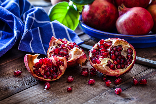 Fresh organic pomegranates on rustic wooden table. The pomegranates are in a blue plate and one is cut in half. A blue napkin is out of focus at background. Some seeds are spilled on the table. Predominant colors are red and blue. Low key DSRL studio photo taken with Canon EOS 5D Mk II and Canon EF 100mm f/2.8L Macro IS USM