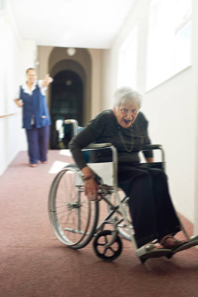 Shot of a mischievous senior woman using her wheelchair to run away form her nurse in an old age home
