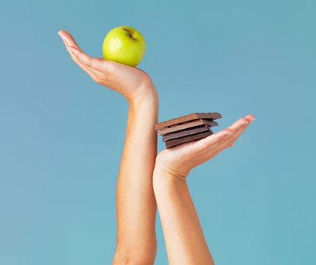 Cropped studio shot of a woman holding up chocolate and an apple against a blue background