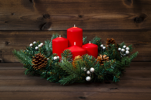 Decorated Advent wreath with four red candles on a wooden background.