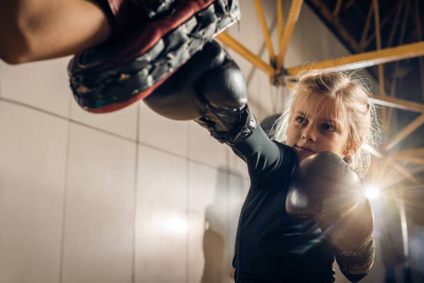 Little boxer having a sports training with her unrecognizable coach in a gym. Small girl exercising boxing with unrecognizable coach in a health club. mixed martial arts photos stock pictures, royalty-free photos & images