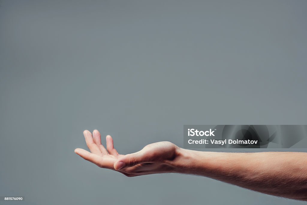 Handsome man on grey background. Man hand isolated on grey background. Holding something from below. Asking for help gesture. Hand Stock Photo