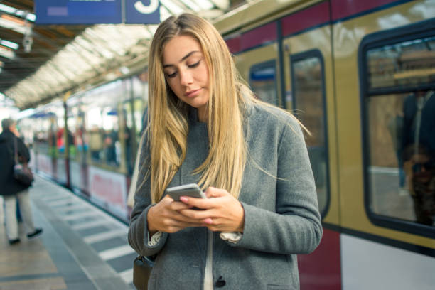 istock Young woman using mobile phone while waiting for train at railway station. 881598162