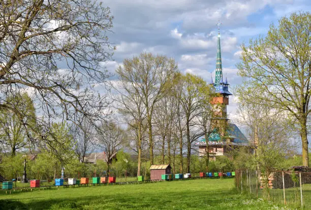 Spring rural landscape with traditional maramures neo-gothic church and multicolor beehives on green meadow in Sapanta village, Romania