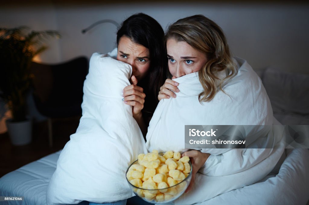 Nightmare Scared girls hiding in blanket while watching horrors on TV at night Movie Stock Photo