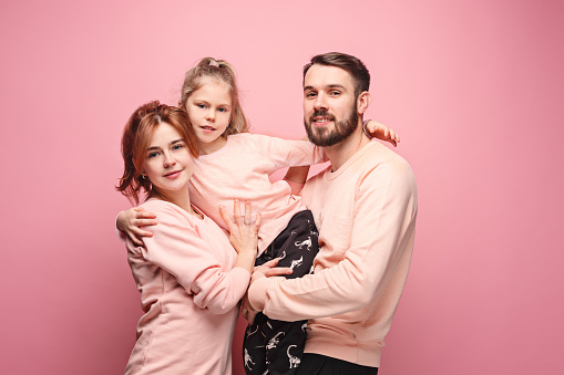 Happy young family with one little daughter posing together on pink studio background