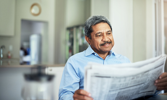 Cropped shot of a senior man reading the morning paper while sitting at home