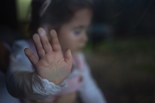 Sad and depressed baby girl is leaning her hand on window