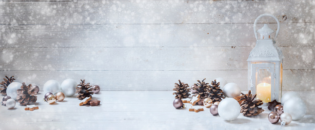 wide christmas background with a candle light lantern, baubles, cinnamon stars, cones and snoe on rustic bright wood, panorama format for website banner, copy space, selected focus