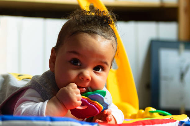 Stock photo of 5 months old baby girl who is playing on the floor mat with toys.