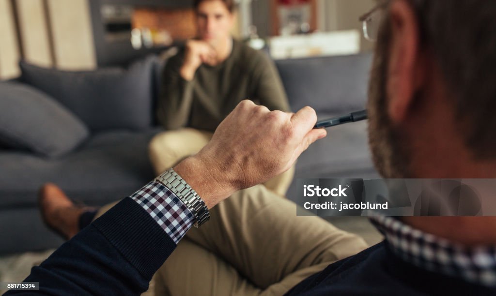 Psychotherapist understanding problems of a male patient Hands of psychologist holding a pen and listening to man during therapy session. Psychotherapist understanding problems of a male patient. Mental Health Professional Stock Photo