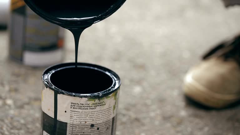 Artist pouring a black paint from can to another can.