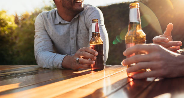 Couple having beers at outdoor party Couple sitting outdoors at wooden table having beers and talking. Focus on couple hands with beer bottles during a outdoor party. beer bottle photos stock pictures, royalty-free photos & images