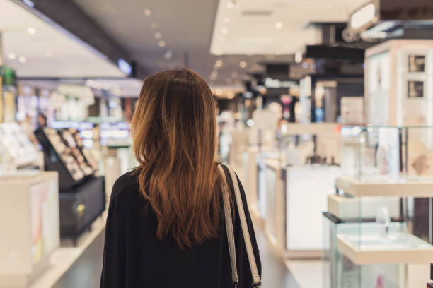 junge asiatische frau, die zu fuß in kosmetik-abteilung in der mall - shopping mall store shopping retail stock-fotos und bilder