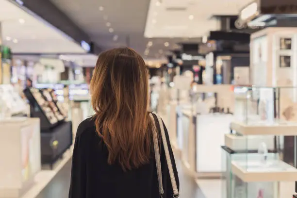 Photo of Young asian woman walking in cosmetics department at the mall