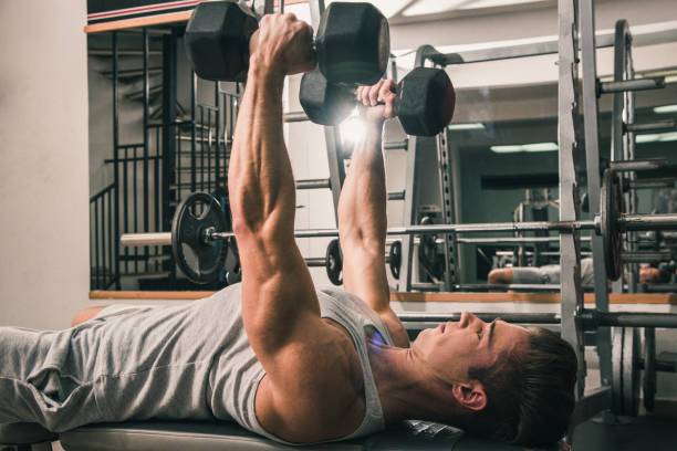 istock Man lying on the gym bench and practicing with hand weights 881794158