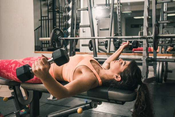 istock Woman lying on the gym bench and practicing with hand weights 881794256